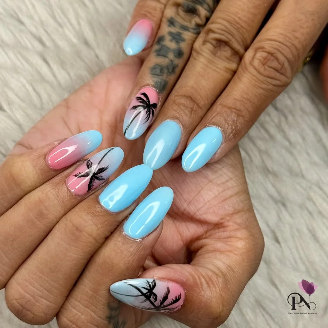 Palm Tree Nail Art A close-up of hands displaying long, oval-shaped acrylic nails featuring a vibrant pink and blue ombre design with black palm tree silhouettes, while the other nails are a solid glossy light blue.